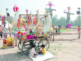 Two children play in the shade of their rehri selling Dussehra items in Parade Grounds, Dehradun, on Monday.
