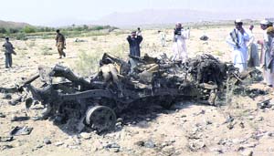 Local residents stand beside the wreckage of a vehicle at the site of a suicide bombing in Baka Khel area near Bannu, Pakistan, on Monday.