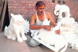 A craftman carves out figurines from thermocol and a thached-roof mud hut ready to display crafts item at Kalagram.