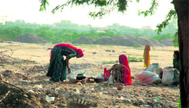 Nomadic women prepare food in the open amidst Gurgaon skyscrapers.