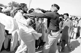 A man, displaced by fighting in South Waziristan, is pulled out of a food distribution line by a policeman on the outskirts of Dera Ismail Khan, on Saturday.