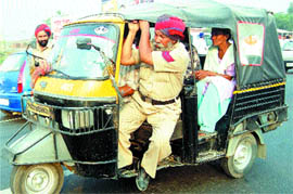 A policeman hangs out of an auto-rickshaw even though the police has banned passengers sitting with driver on front seat.