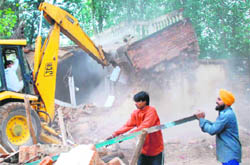 The demolition squad of the enforcement wing razes illegal structures at Sector 55, Chandigarh, on Monday. 