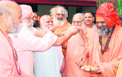 Members of the Akhara Parishad distribute sweets after a consensus among different akharas was arrived at in Haridwar late Saturday evening.