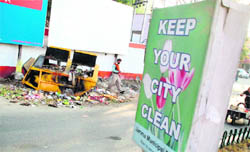 An overflowing garbage bin near a Municipal Corporations signboard appealing to people to keep the city clean.