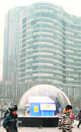 People walk past Christmas decorations in a bubble at a shopping plaza in Beijing as a new high-rise building nears completion (background)