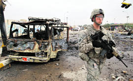 A US soldier walks past a damaged bus at the site of a bomb blast in northern Baghdad on Tuesday