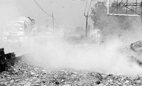 Smoke from dumped garbage causes pollution and hampers visibility, forcing vehicles to switch on lights near DAV School in Derabassi on Saturday. 
