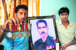Vikrant Singh (left) and his cousin Mohan Pratap Singh with the medals and portrait of their grandfather Budhi Singh at their residence in Suchani.