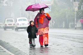 A woman walks with her child as rains lash Dehradun city
