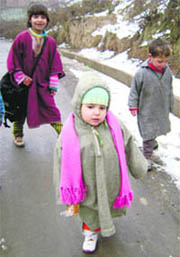 Children in pherans walk on a Srinagar street as the temperature fell following a heavy snowfall on Sunday.