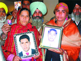 Joginder Kaur and Jeet Kaur hold photographs of their sons, with parents of other boys, who went missing en route to Spain in 2004