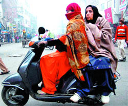 Women take full protection against cold as they ride a scooter on a chilly day, in Amritsar on Wednesday