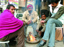 Some dailywagers sit huddled around a fire to keep themselves warm, in Jalandhar