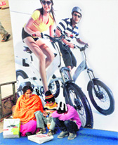 A women sits with her children in front of a poster at Auto Expo in New Delhi on Sunday.