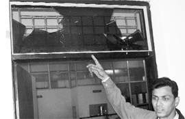 An employee shows a broken windowpane after an attack at Gurukul Vidyapeeth on Sunday.