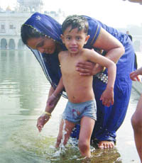 A woman bathes her child on the occasion of Makar Sankranti at Gurdwara Bangla Sahib in New Delhi on Thursday.