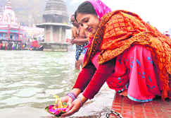 A devotee offers a lamp to the Ganga on Saturday morning; and a police officer on duty at the Kumbh Mela area in Haridwar.