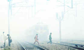 People cross railway tracks amidst heavy fog at Shivaji Bridge Railway Station in New Delhi on Sunday.
