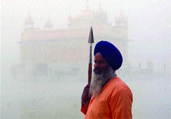 An SGPC task force man stands guard in front of the barely visible Golden Temple on a foggy Monday in Amritsar.