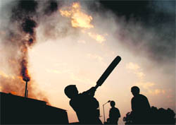Industrial chimneys billow out thick smoke in the Industrial Area at Chandigarh as children have a game of cricket oblivious to the damage this pollution causes to their health and the environment at large