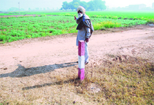 A farmer shows his fields with standing crops, which are to be acquired to set up industry in Khangesra village near Panchkula. A pillar behind the farmer indicates the land purchased by private builders in the area. 