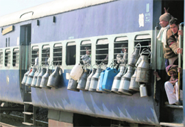 Milkmen stand guard as their containers hang out from a coach of a passenger train passing through a village in Gurgaon district.