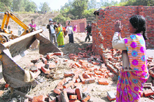 A woman pleads as a Dehradun Municipal Corporation bulldozer demolishes illegal structures at Brahamawala in Dehradun on Wednesday. 