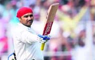 Virender Sehwag raises his bat after completing his century on Monday.