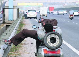 A man spends some leisure time on his scooter parked on the Delhi-Gurgaon Expressway where the entry of two-wheelers is banned