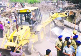 A JCB machine tears down illegal structures during a demolition drive by GMADA in Phase I, Mohali