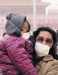 Tourists wearing face masks stand amid a sandstorm on Tiananmen Square in Beijing
