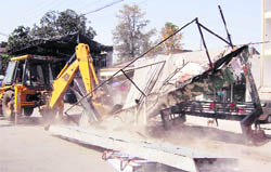 A bulldozer of the Dehradun Municipal Corporation demolishes an illegal hoarding put up near the main 