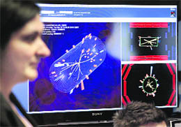 A scientist stands in front of pictures of the first successful collisions at full power at the Compact Muon Solenoid (CMS) experience control room of the LHC at CERN in Meyrin, near Geneva 