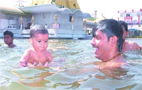A man along with his child takes a holy dip in a sarovar at Devi Talab Mandir on Baisakhi in Jalandhar
