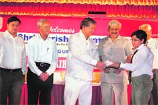 Harish Rawat gives a scholarship cheque to a student at Graphic Era University on Sunday.