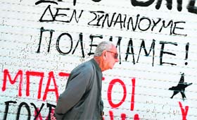 A man walks in downtown Athens on Sunday next to a slogan reading We do not agree  We have war'