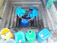 Women lift water from a dried-up baoli to fill their cans at a village.