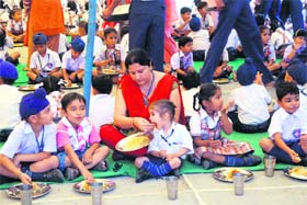 A teacher feeds a student at a community kitchen during the birth anniversary celebrations of the founder principal of Shiksha Niketan Higher Secondary School at Jeev Nagar in Jammu