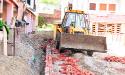 A bulldozer breaks the boundary wall of a school at Khadkhadi 