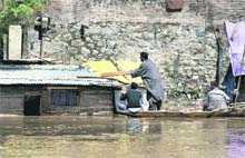 A man puts a log over a tin sheet to prevent it from damage as water from the Jhelum submerges his house at Habbakadal in Srinagar on Wednesday. 