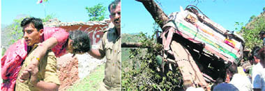 Security men carry a woman who was injured in a bus accident in Bidda village, Reasi, on Friday, to hospital; and (right) the mangled remains of the ill-fated bus that fell into the gorge.