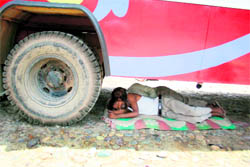 The driver and conductor of a private bus take a nap under the vehicle to beat the heat in Nagrota on Sunday. 