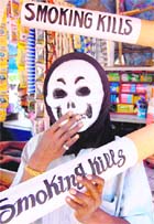 An activist wearing a skull mask displays an oversize cigarette with tobacco warning message at a pan shop on the eve of World No Tobacco Day in Karad, Maharashtra, on Sunday.
