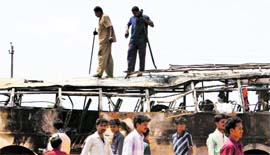 People look at the remains of a burnt bus in Challakere, Karnataka, on Sunday.