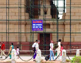 Visitors walk past a CPWD board that warns of danger due to construction work at the India Gate in New Delhi on Sunday.