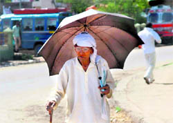 An old man uses an umbrella to save himself from the scorching heat at Satwari Chowk in Jammu