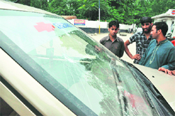 people look on at the damaged windshield of the vehicle of the Tribune team that was broken in stone throwing at Avantipora