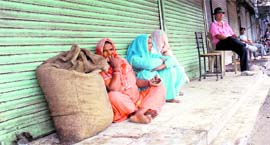 Women sit outside a closed shop in Karnal on Monday.