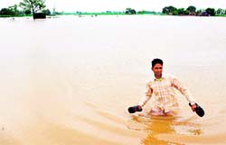 A farmer wades through his flooded field in Urna village